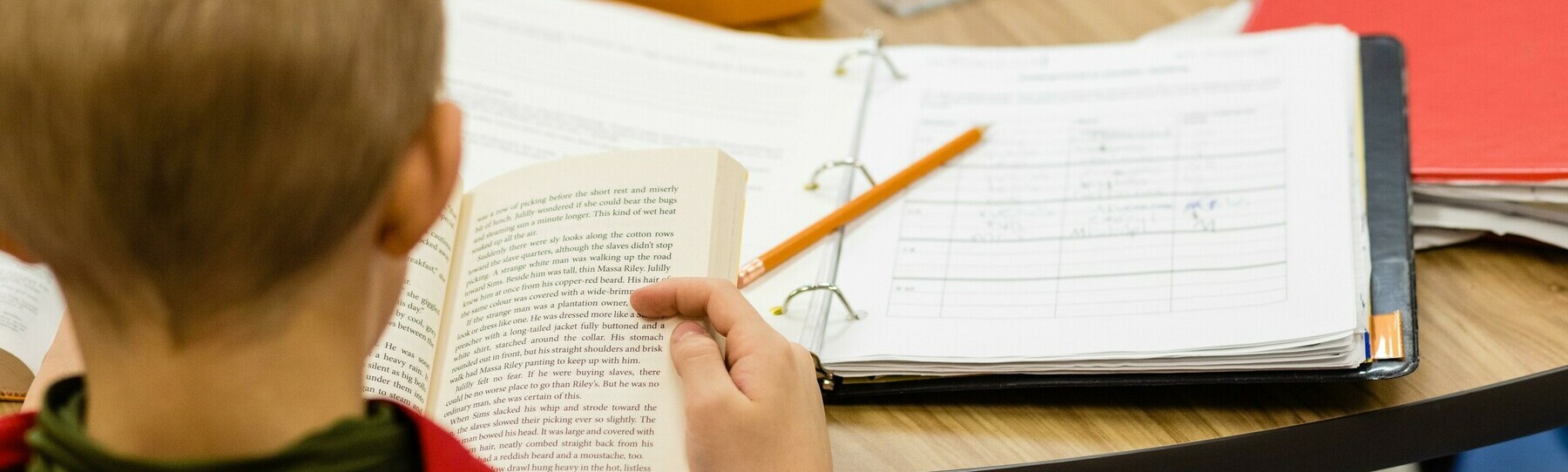 Student reading a book at a table doing schoolwork